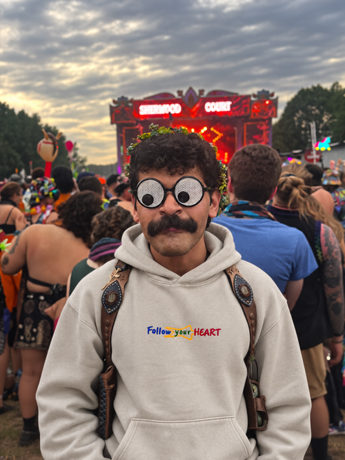 Man in the Follow your Heart ivory hoodie in front of a festival stage