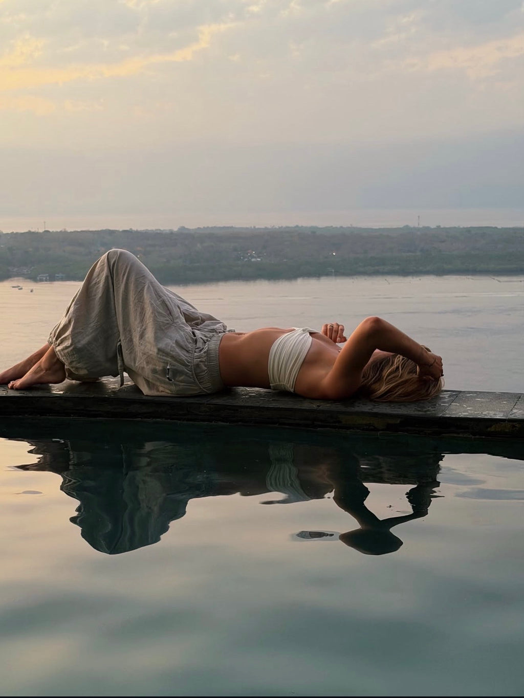 Woman lying on the edge of an infinity pool in Linen Love Pants at sunset